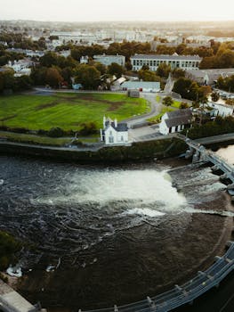 Aerial shot of a river, lush greenery, and buildings in County Clare, Ireland at sunset.