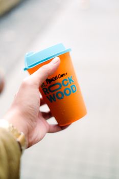 Close-up of hand holding vibrant orange cup with blue lid, perfect for cafe-themed content.
