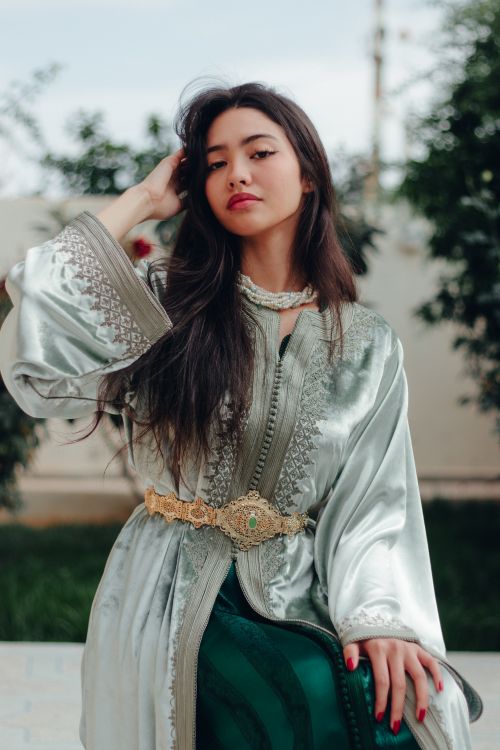 Free Fashionable woman in a silver kaftan with jewelry, sitting outdoors. Stock Photo