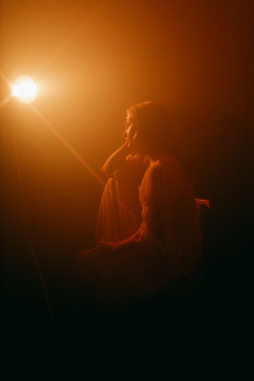 Free Artistic portrait of a woman bathed in warm, dramatic lighting creating a moody atmosphere. Stock Photo