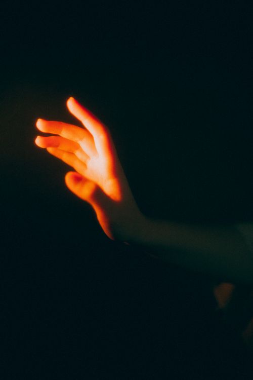 Free A hand illuminated by warm light against a dark background, creating a mysterious glow. Stock Photo