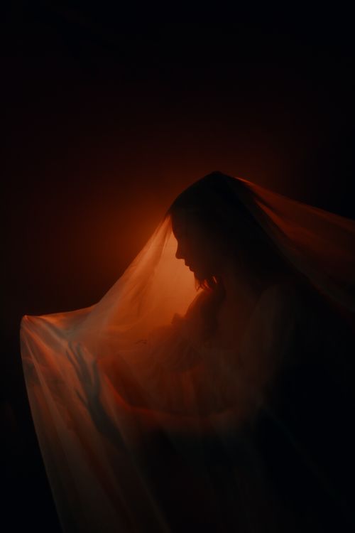 Free Ethereal silhouette of a woman draped with a translucent veil, illuminated by warm light. Stock Photo