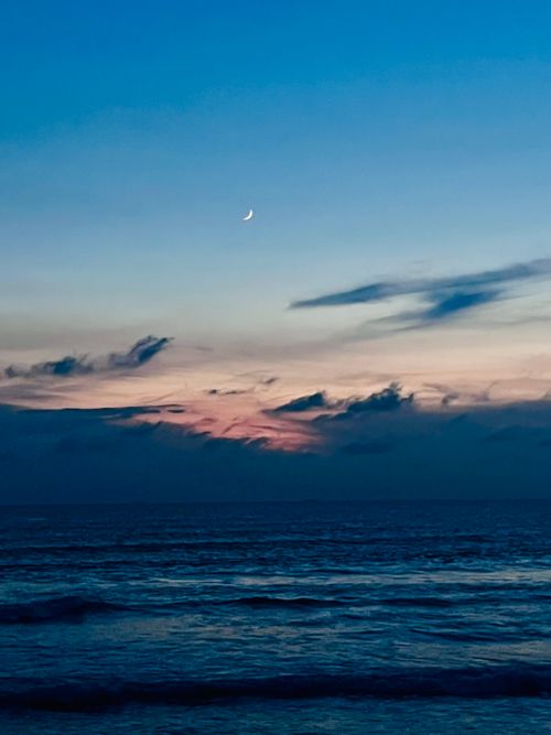 Free Peaceful ocean view with crescent moon against pastel twilight sky. Stock Photo