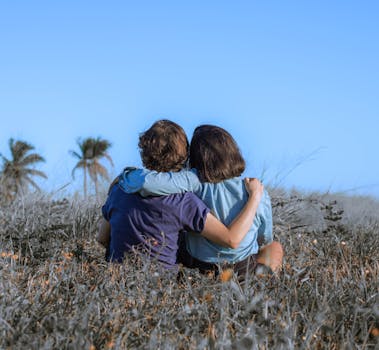 一对夫妇坐在草地上，在晴朗的蓝天下相拥