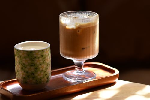 Free A cozy scene with iced coffee in a glass and hot tea in a floral cup on a wooden tray. Stock Photo
