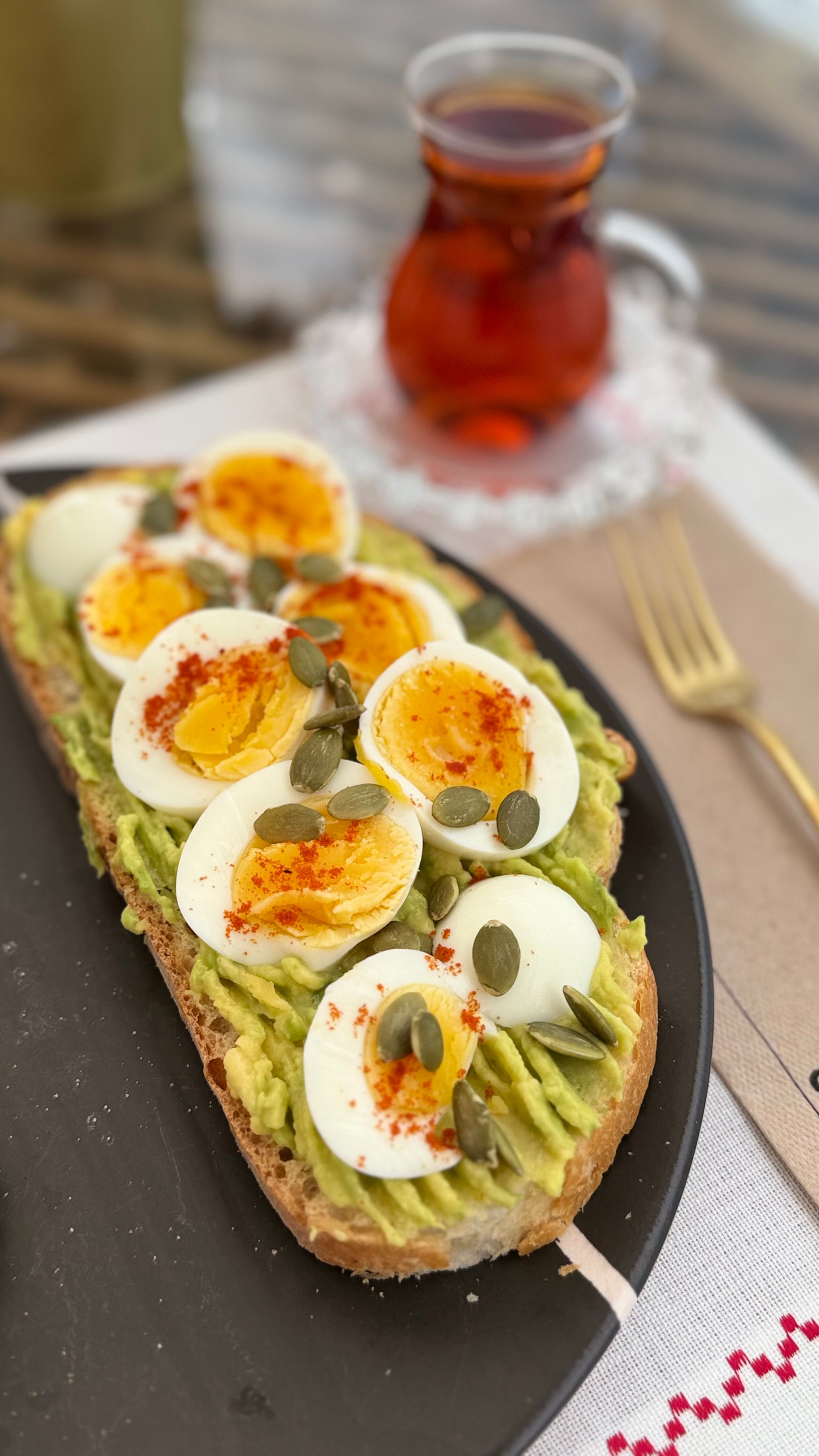 Delicious avocado toast topped with sliced boiled eggs, pumpkin seeds, and paprika served with tea.