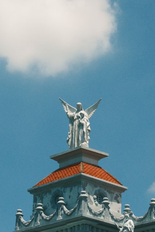 Free Majestic angel statue atop a detailed building facade against a vibrant blue sky and clouds. Stock Photo