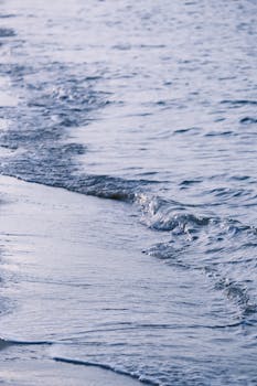 Gentle sea waves lapping onto a sandy beach under soft daylight, evoking peace.
