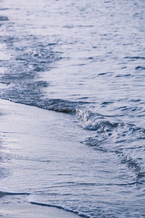 Free Gentle sea waves lapping onto a sandy beach under soft daylight, evoking peace. Stock Photo
