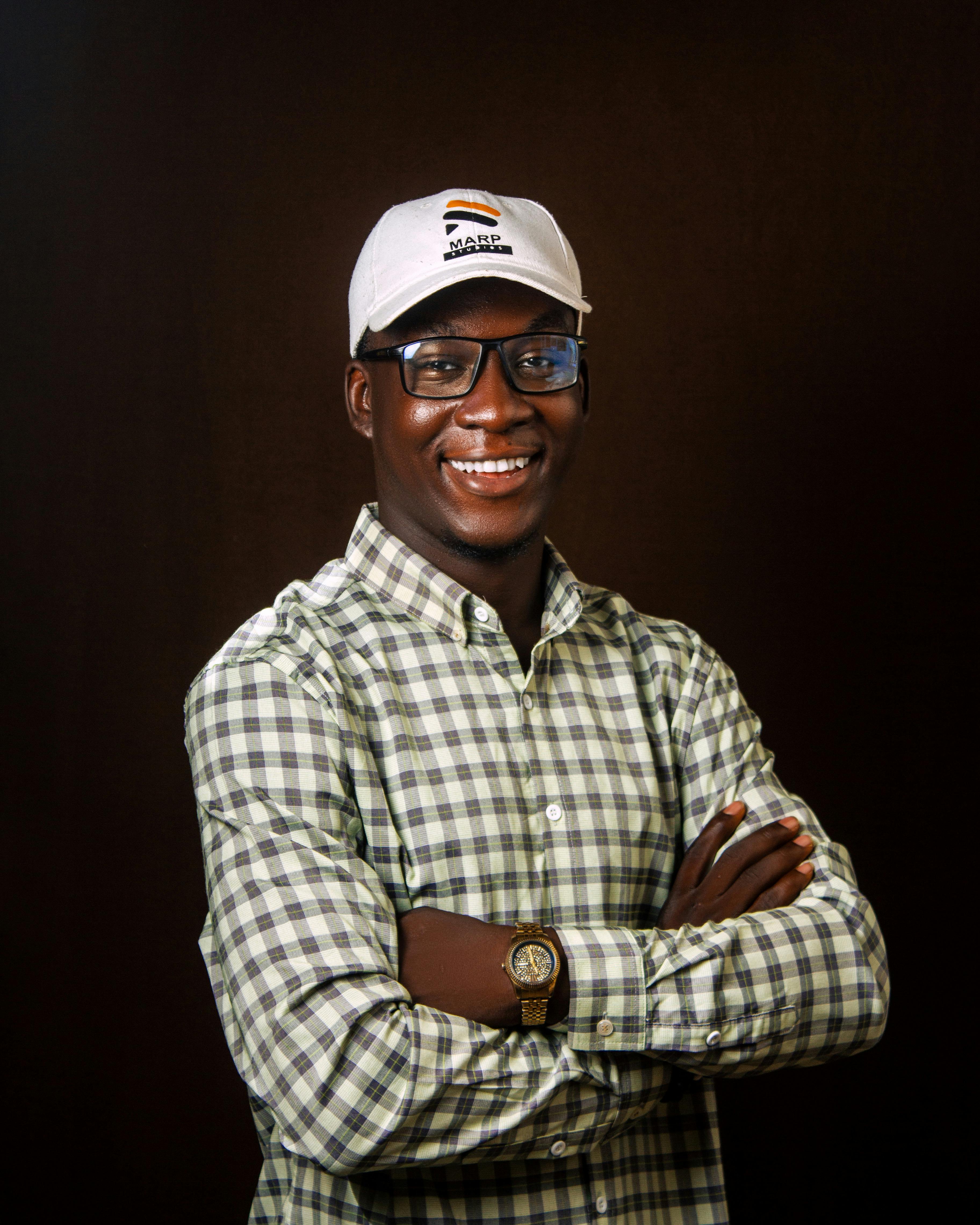 Smiling man in plaid shirt and cap with glasses posing confidently.