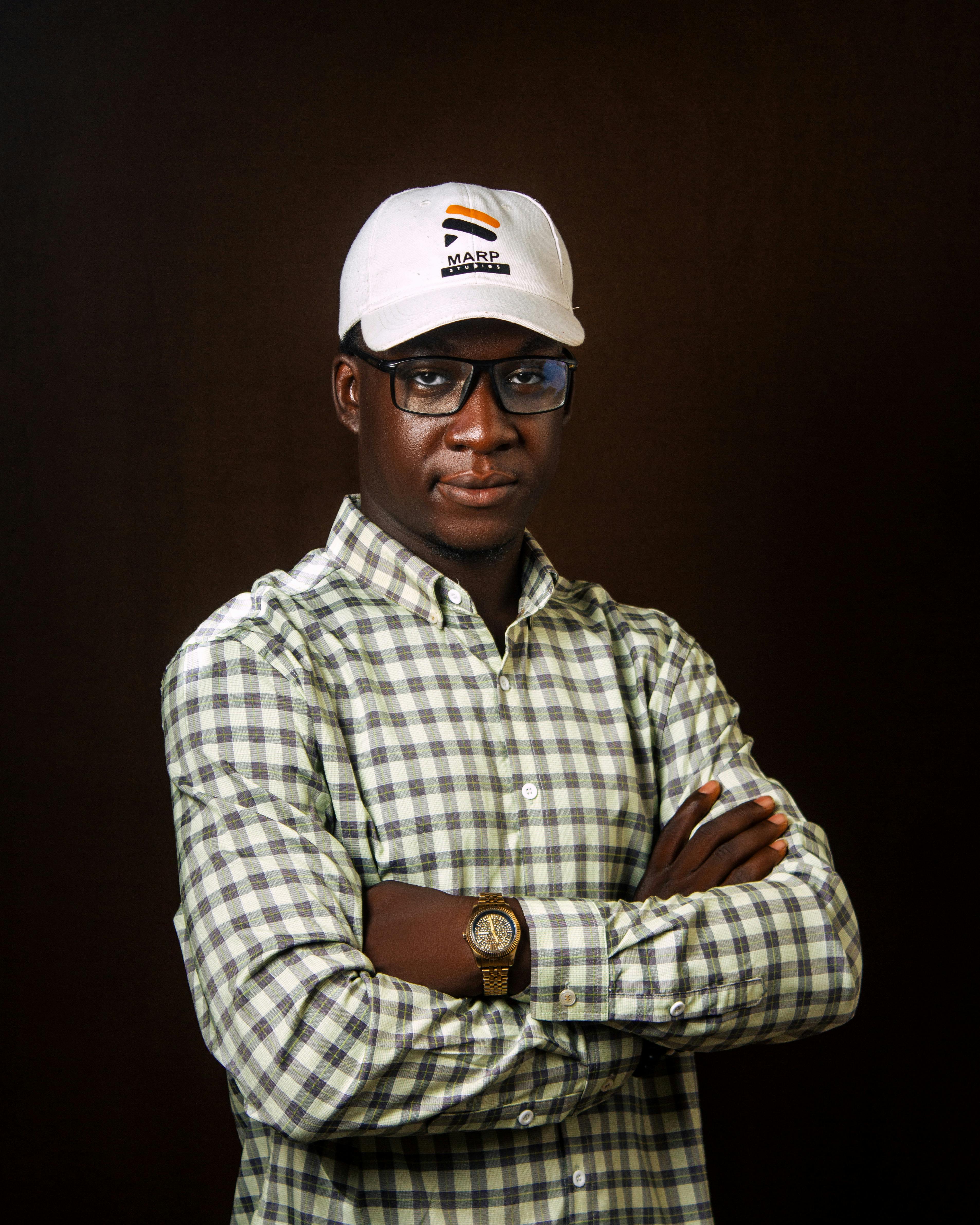 Portrait of a confident man wearing a checkered shirt and cap against a dark background.