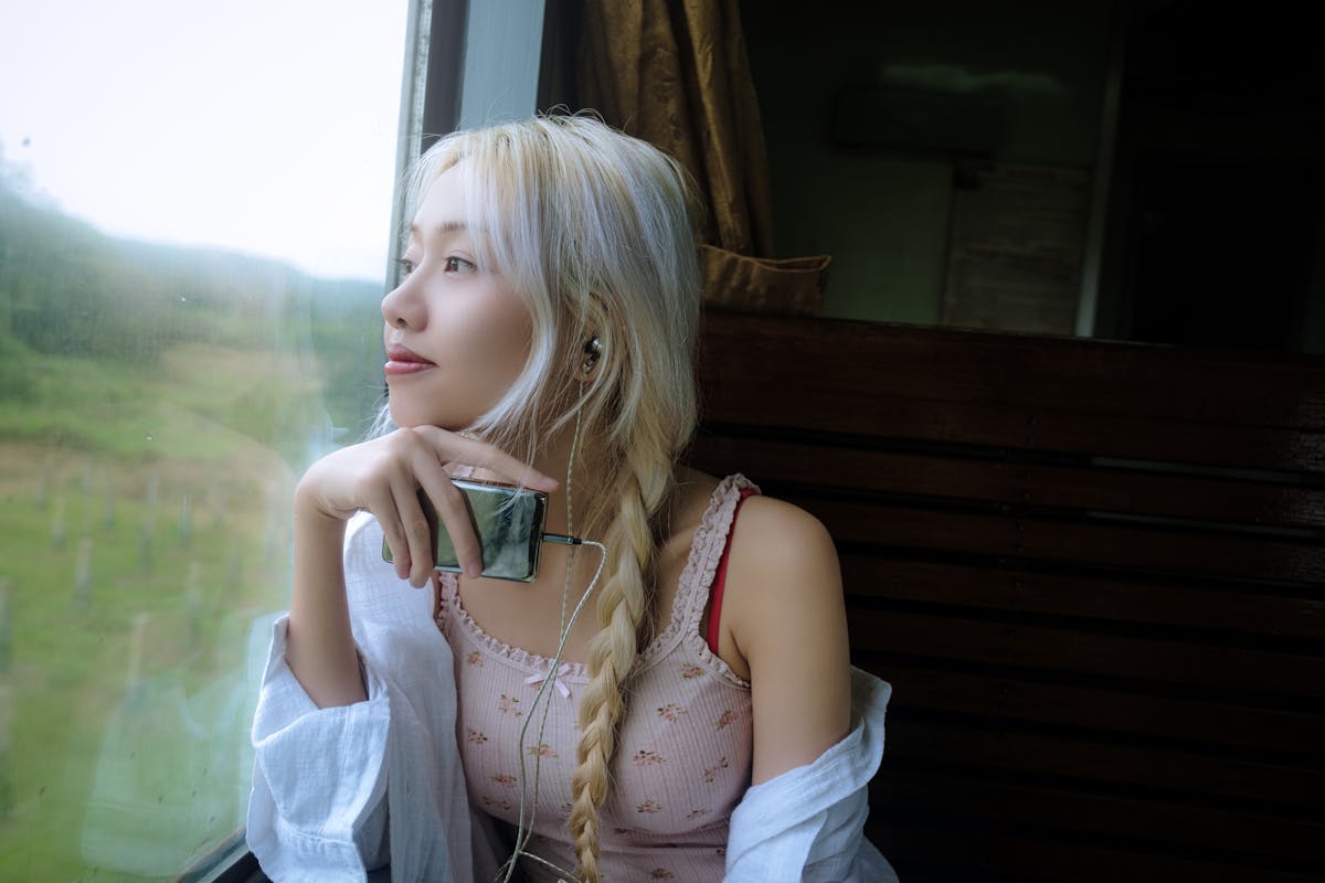 Persona con cuffie che guarda fuori dal finestrino di un treno, espressione pensierosa