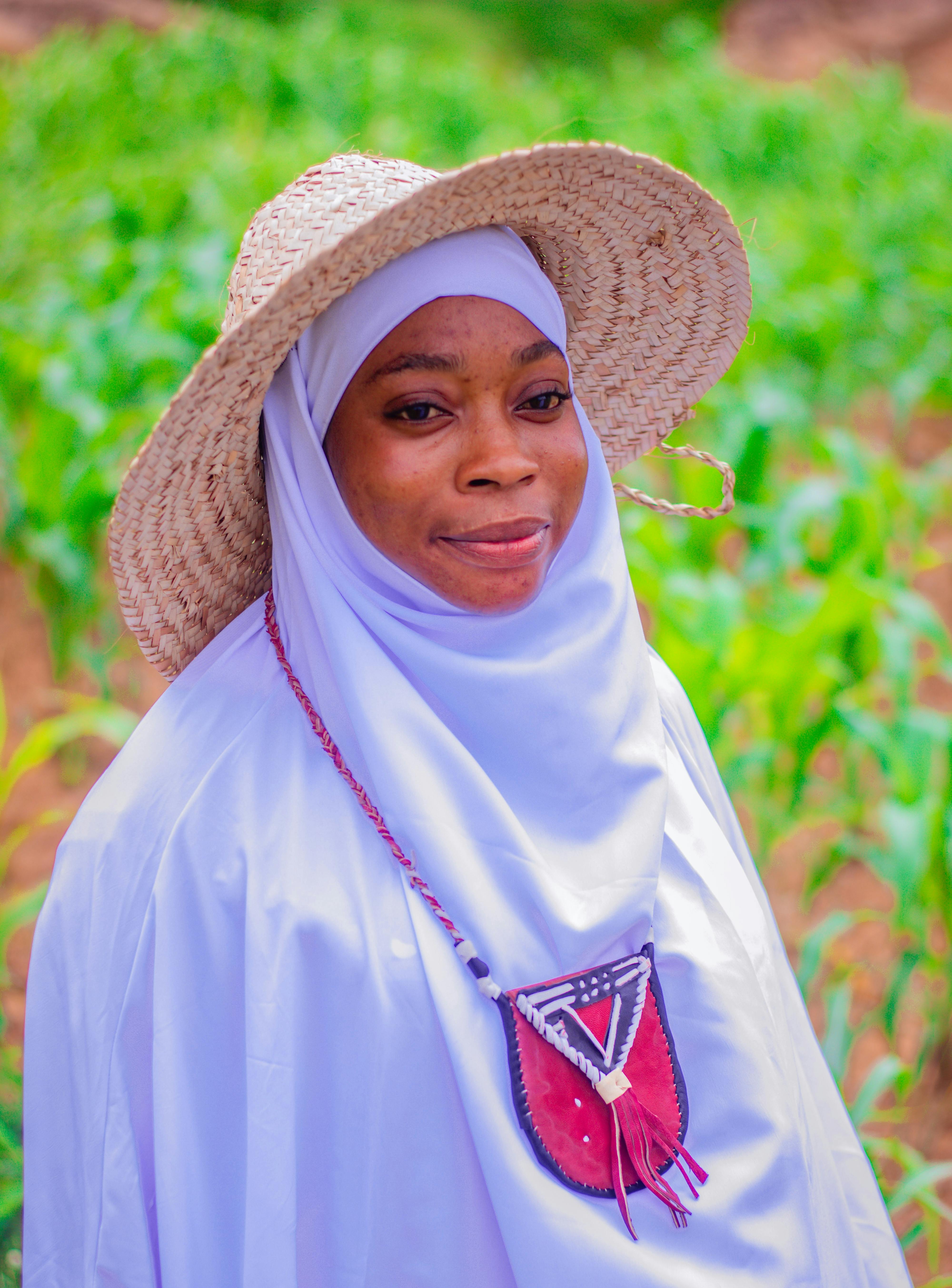 Smiling woman in traditional attire with straw hat, outdoors in a green field.