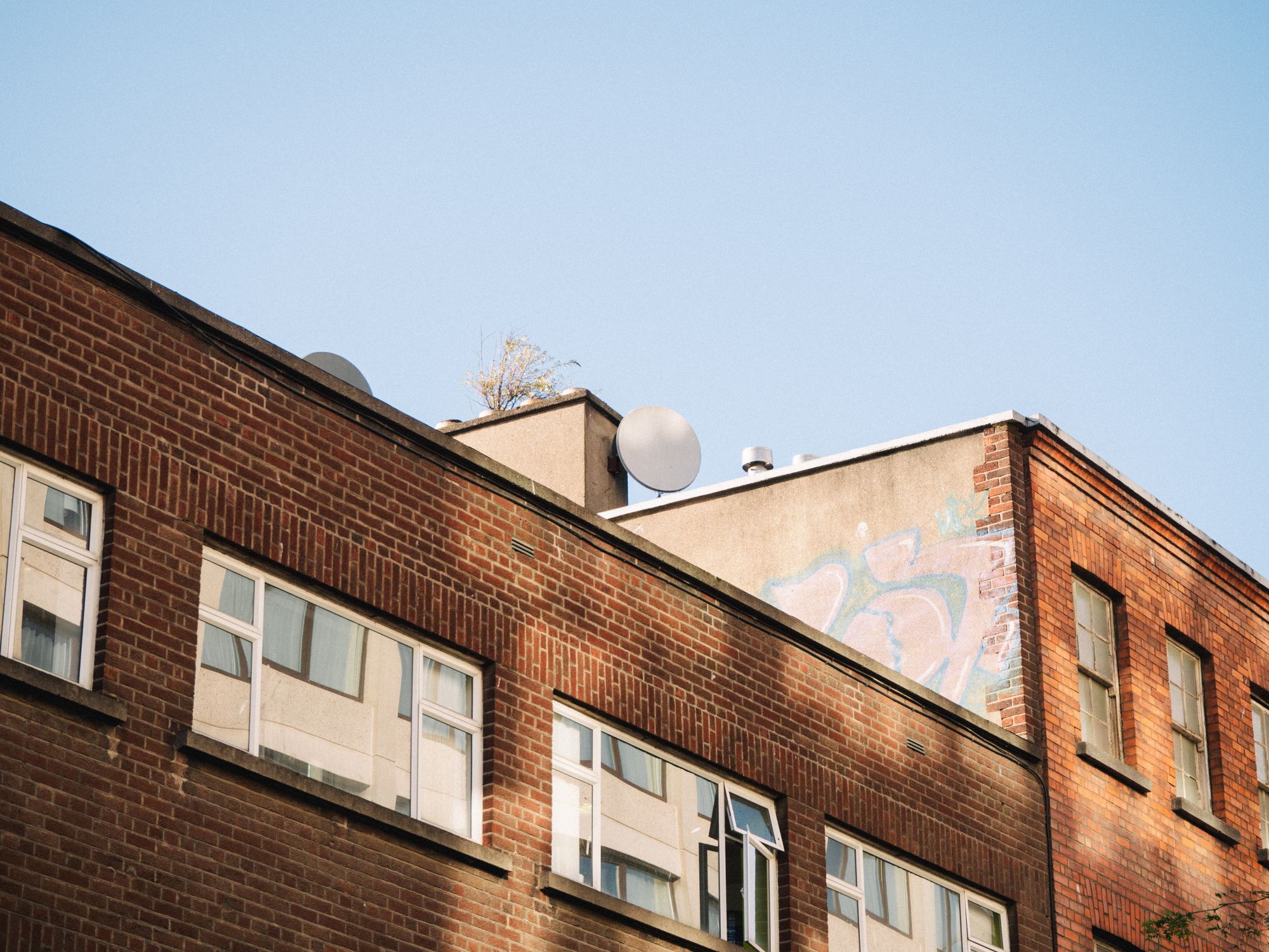 Urban brick building with satellite dish and graffiti under a clear blue sky in Dublin, Ireland.