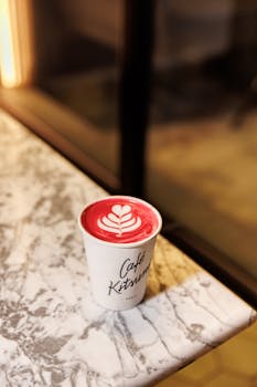 A beautifully crafted red latte with latte art in a Café Kitsuné cup on a marble table.
