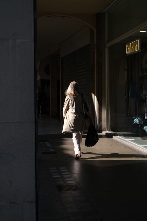Free A woman with a bag walks through a shadowy arcade in Padova, Veneto, Italy. Stock Photo