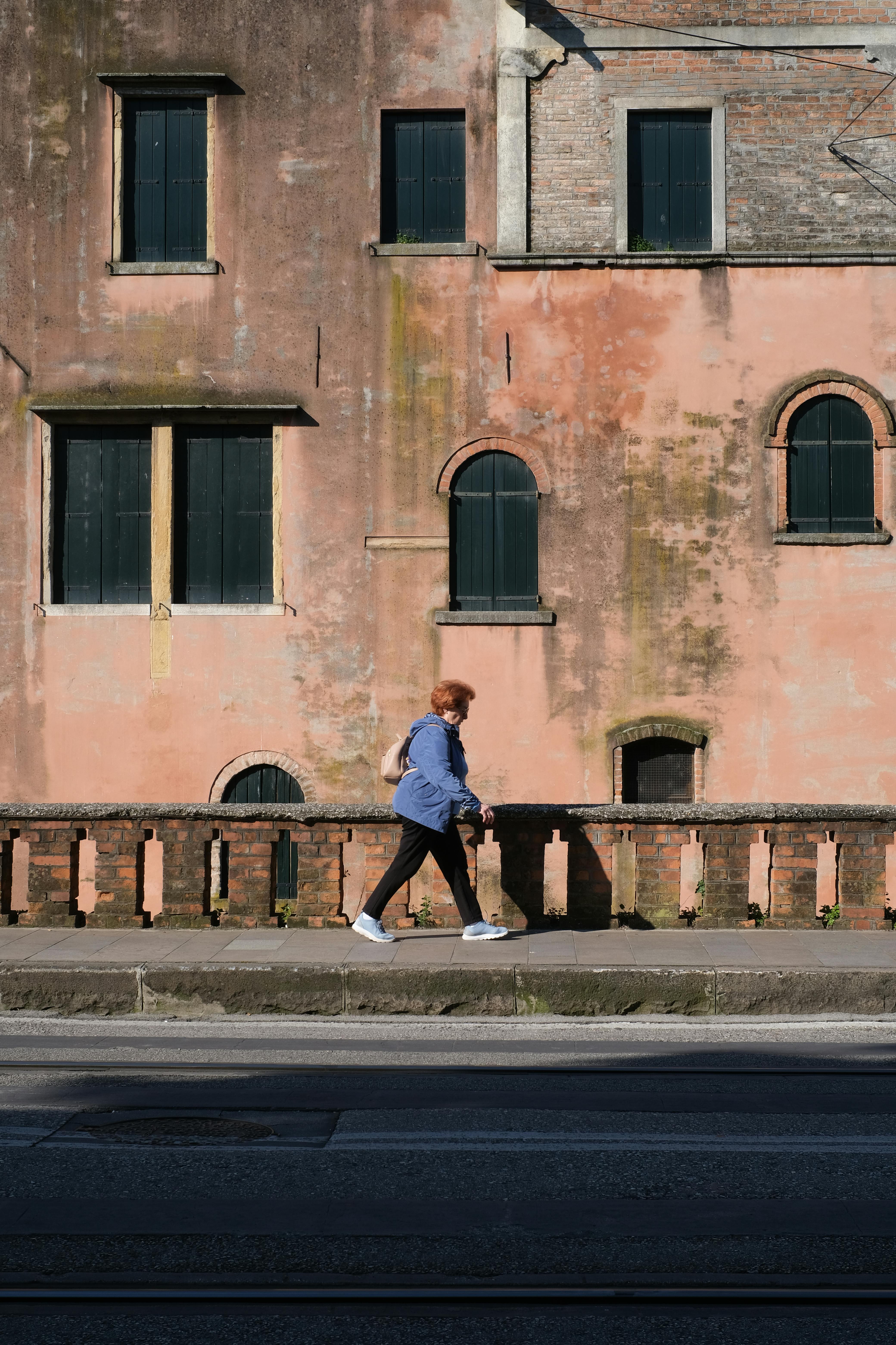 A woman walking by a rustic wall in historic Padova, capturing the charm of Veneto, Italy.