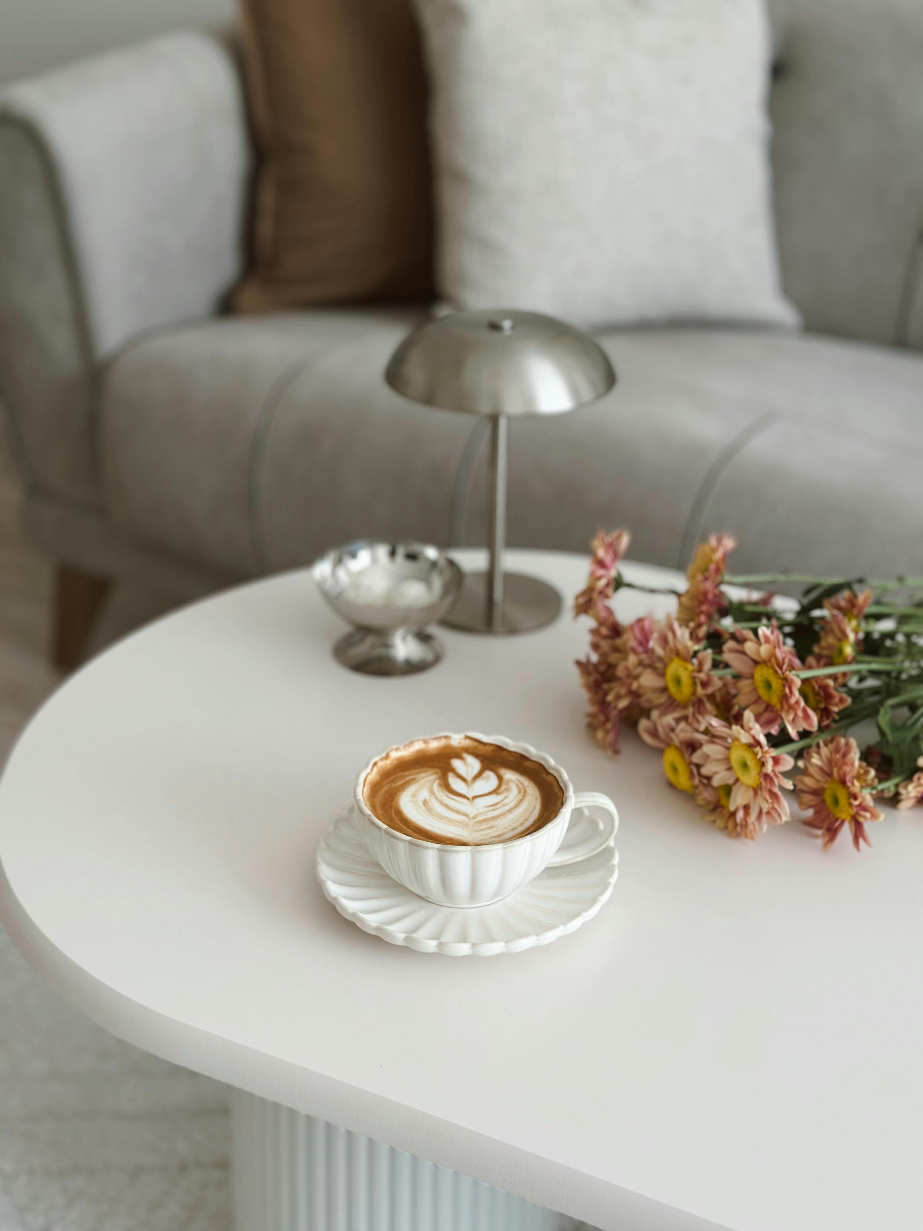 A warm living room scene featuring a latte, flowers, and elegant decor on a white table.