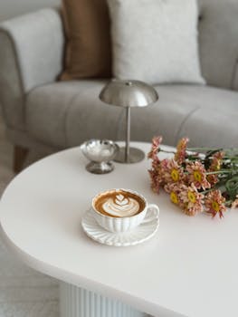 A warm living room scene featuring a latte, flowers, and elegant decor on a white table.