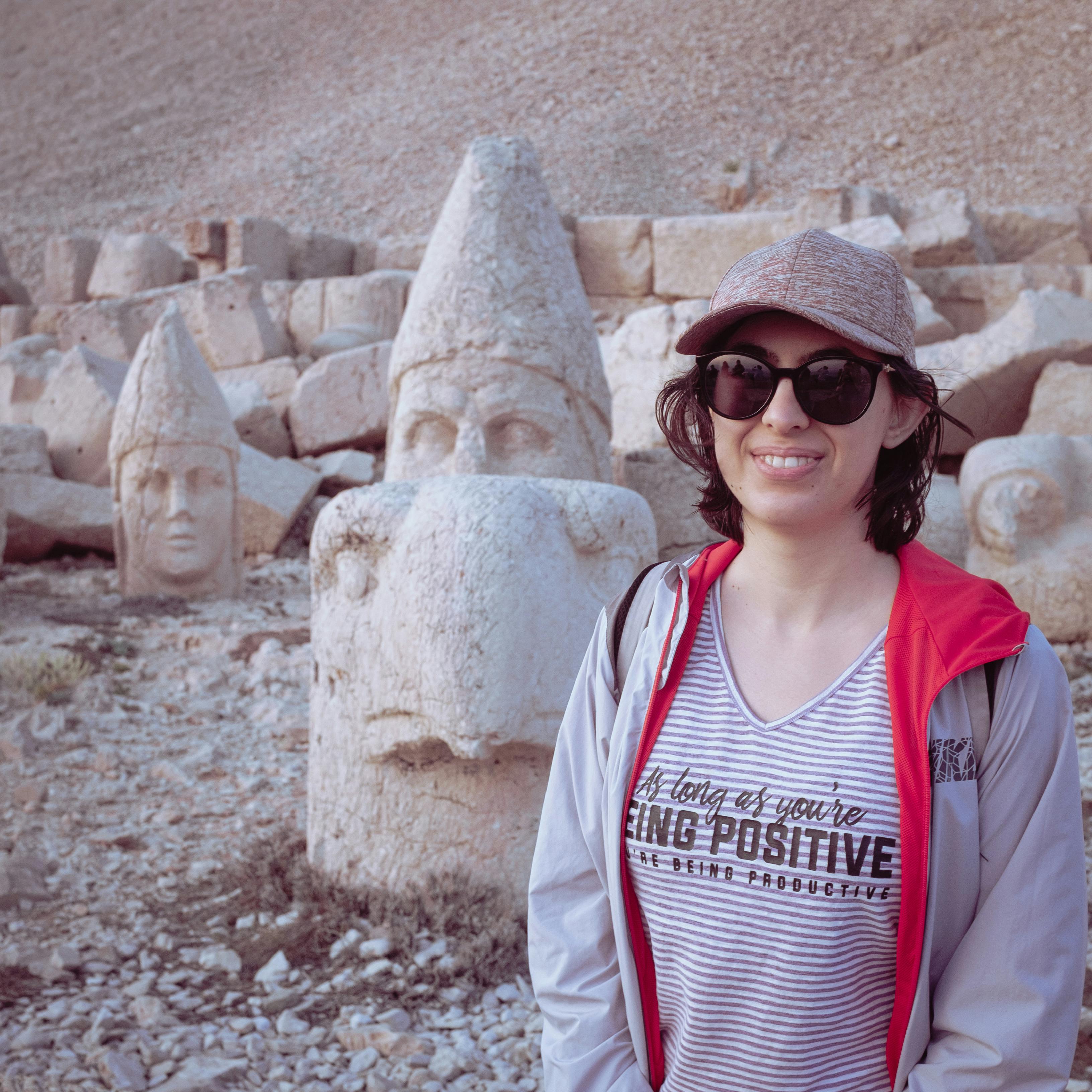 A woman smiles in front of ancient stone heads at Mount Nemrut, Turkey.