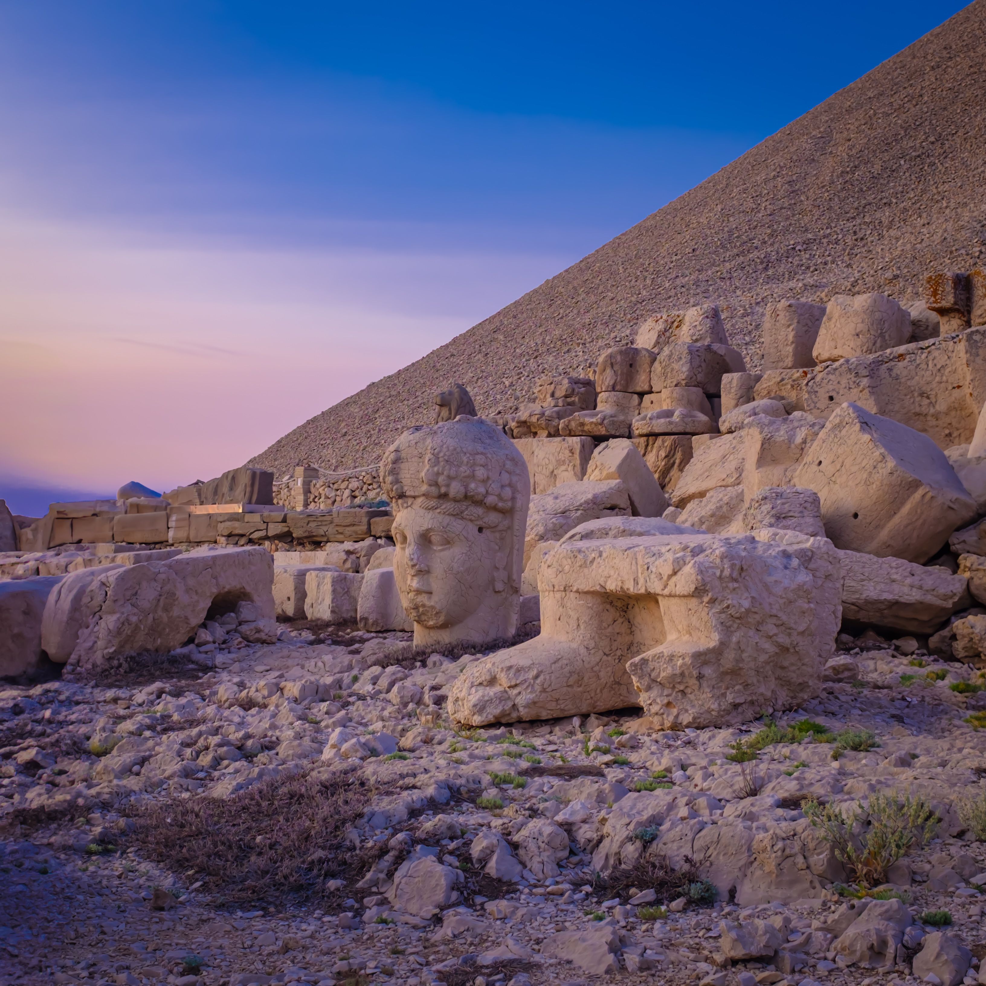Luz do amanhecer sobre cabeças de pedra antigas e ruínas no Mount Nemrut em Adıyaman, Turquia, com o santuário no cume atrás delas.