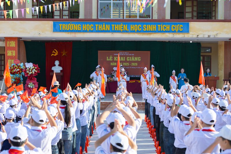 A vibrant school ceremony in Vietnam featuring students in white uniforms and hats waving flags.