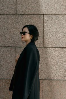 时尚女性佩戴太阳镜，站在有纹理的花岗岩墙旁。 - 相关推荐