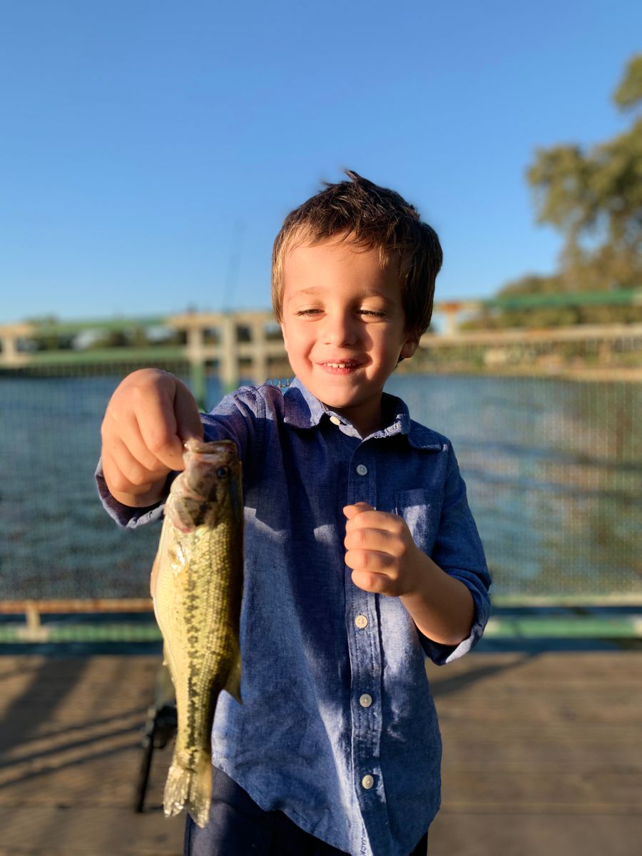 A smiling boy proudly holding up a bass he caught off a dock