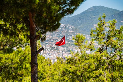 A vibrant aerial shot of the Turkish flag amid green pines above Alanya cityscape, Türkiye.