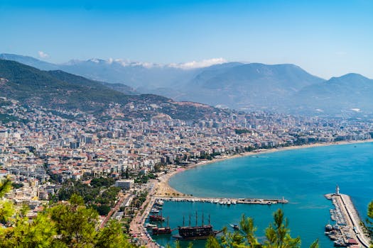 Breathtaking aerial view of Alanya featuring the city, azure sea, and distant mountains under a clear blue sky.