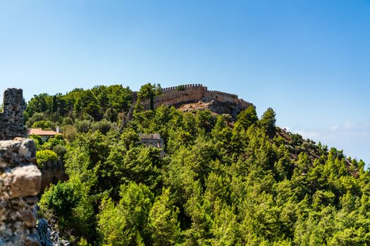 Explore the ancient Alanya Castle in Türkiye set against lush green hills and a clear blue sky.