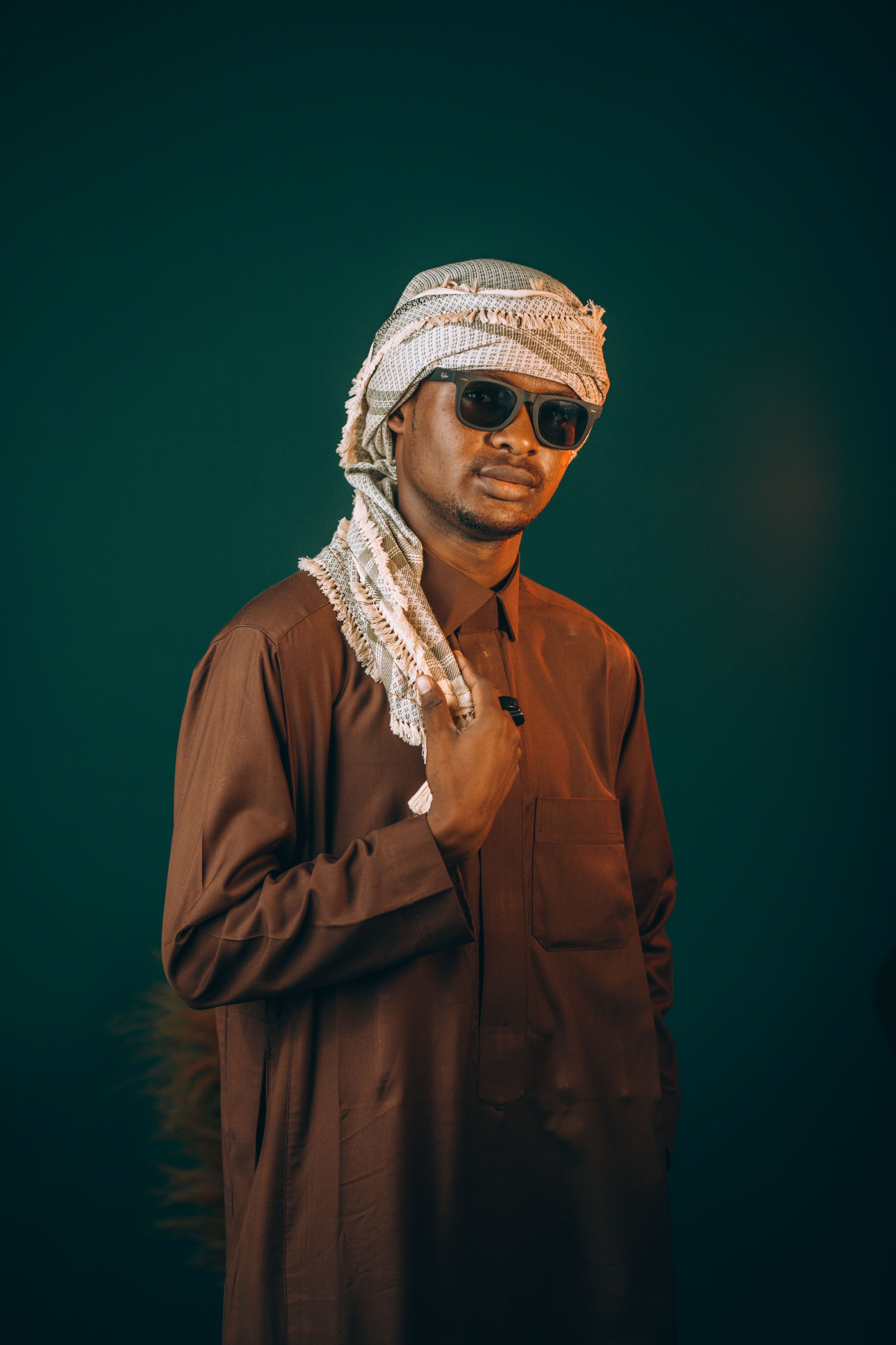 Portrait of a Middle Eastern man wearing a traditional outfit and sunglasses against a green background.