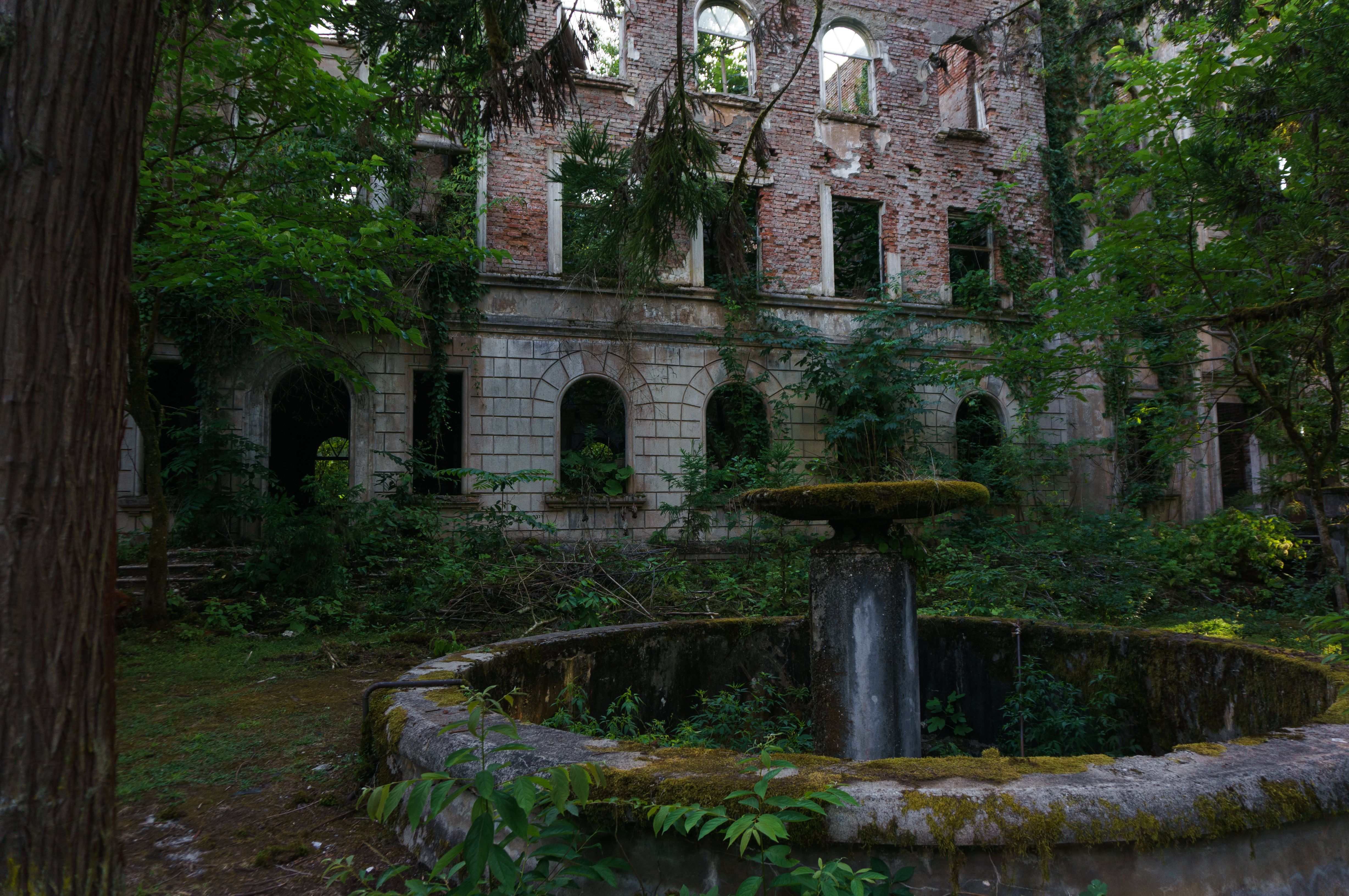 Deserted brick building with an overgrown outdoor fountain and lush greenery in Abkhazia.