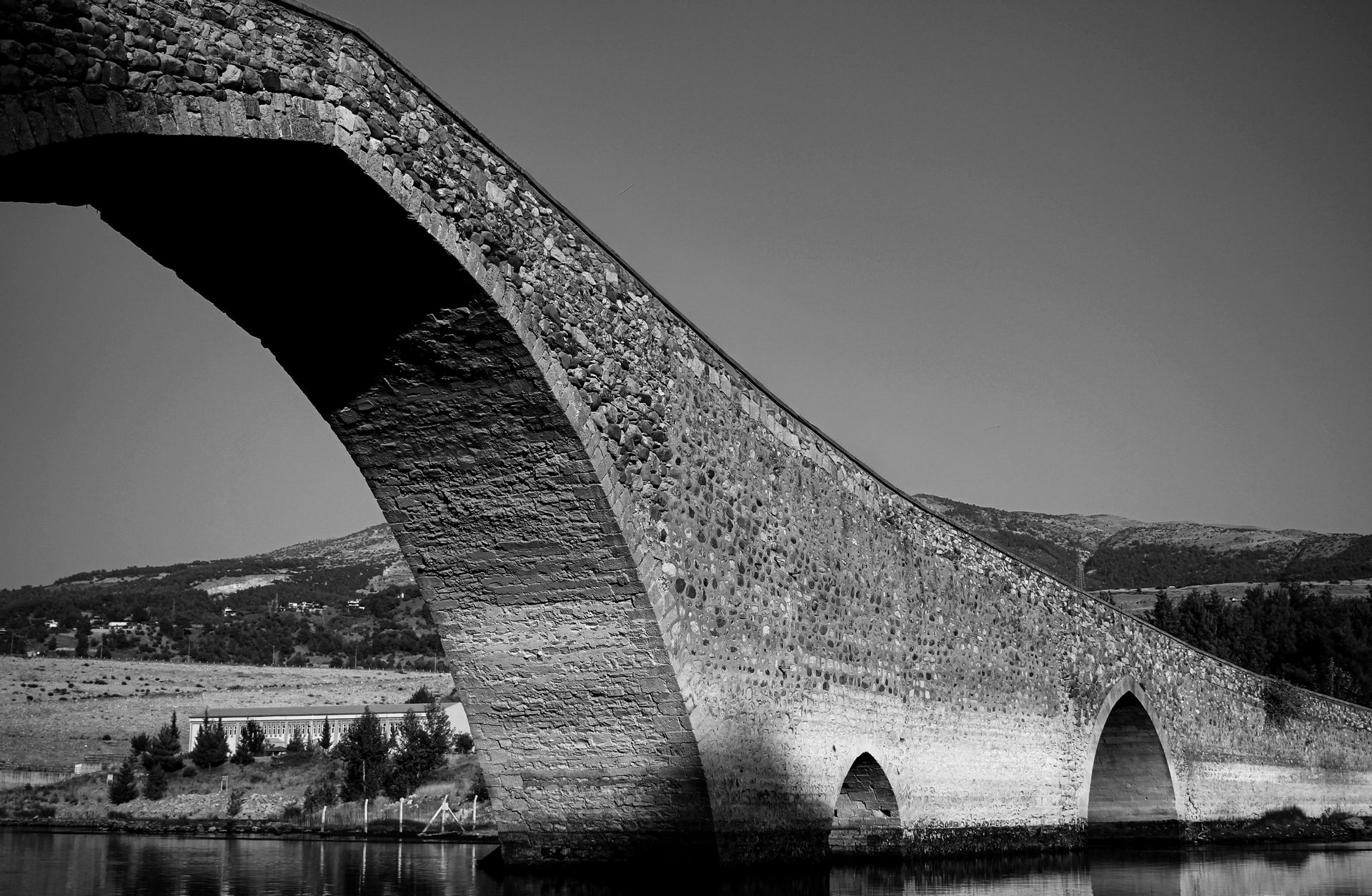 Monochrome photo of a historic stone bridge arching over a river in Kahramanmaraş, Türkiye.