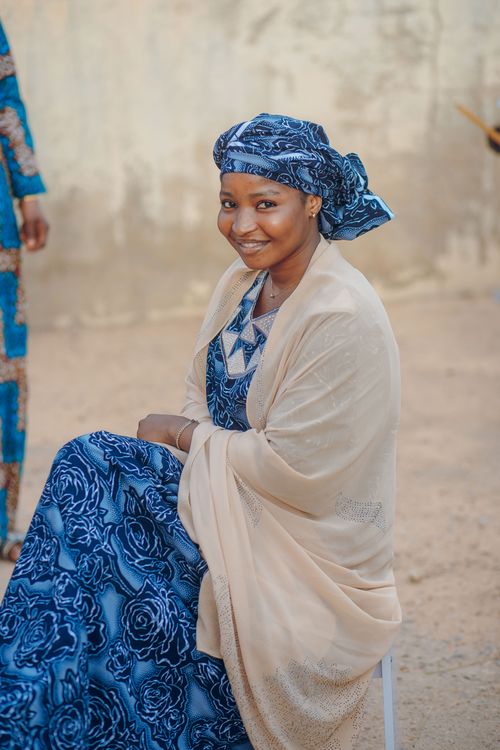 Free Smiling Nigerian woman wearing traditional blue attire and beige shawl outdoors. Stock Photo