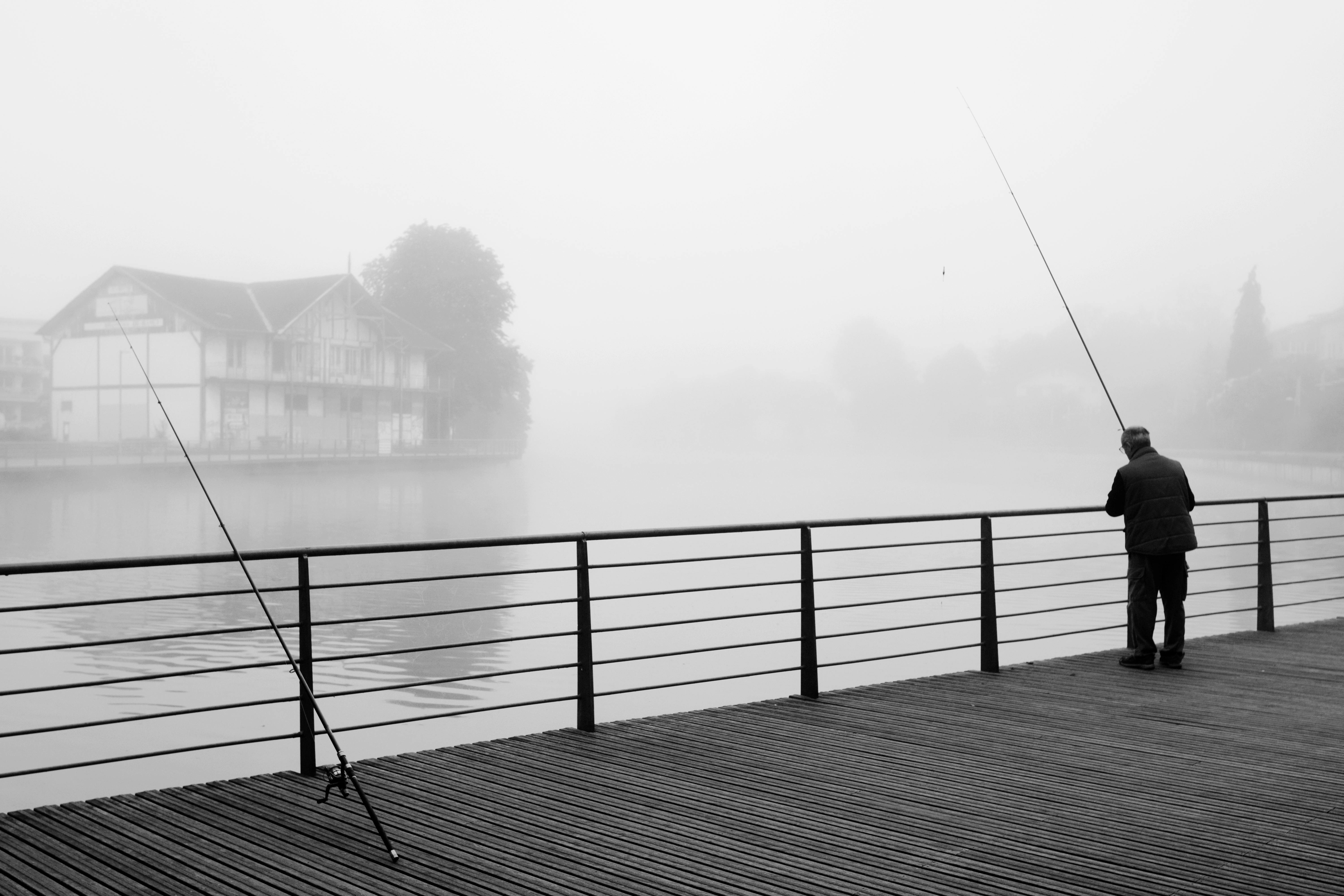 Serene black and white scene of a man fishing by the misty riverside in France.