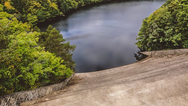 A stunning aerial view showcasing dense forests surrounding a tranquil lake, with a concrete path leading to the water's edge.
