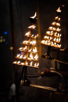 Vibrant display of illuminated brass oil lamps burning with flames during a nighttime ceremony.
