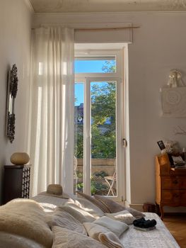 Cozy sunlit bedroom with elegant furnishings and balcony view, perfect for relaxation.