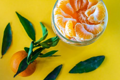 Free Vibrant image of peeled mandarin oranges in a glass bowl with leaves, set against a yellow background. Stock Photo
