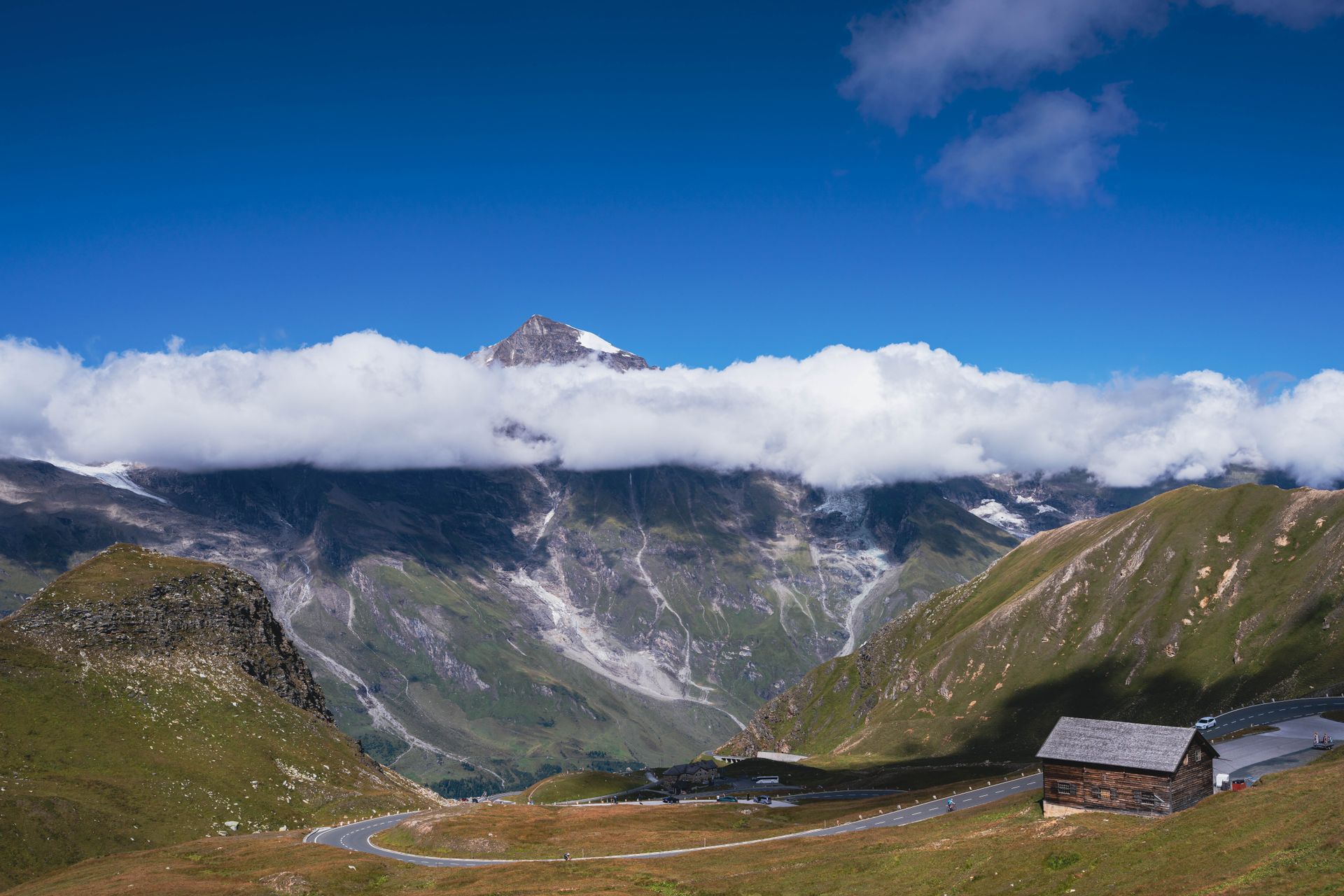Breathtaking view of Alpine mountains with clouds hovering near the peaks, clear blue sky above.
