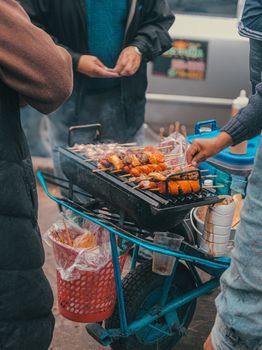 Vibrant street food scene with vendor grilling skewers on a portable barbecue stand.