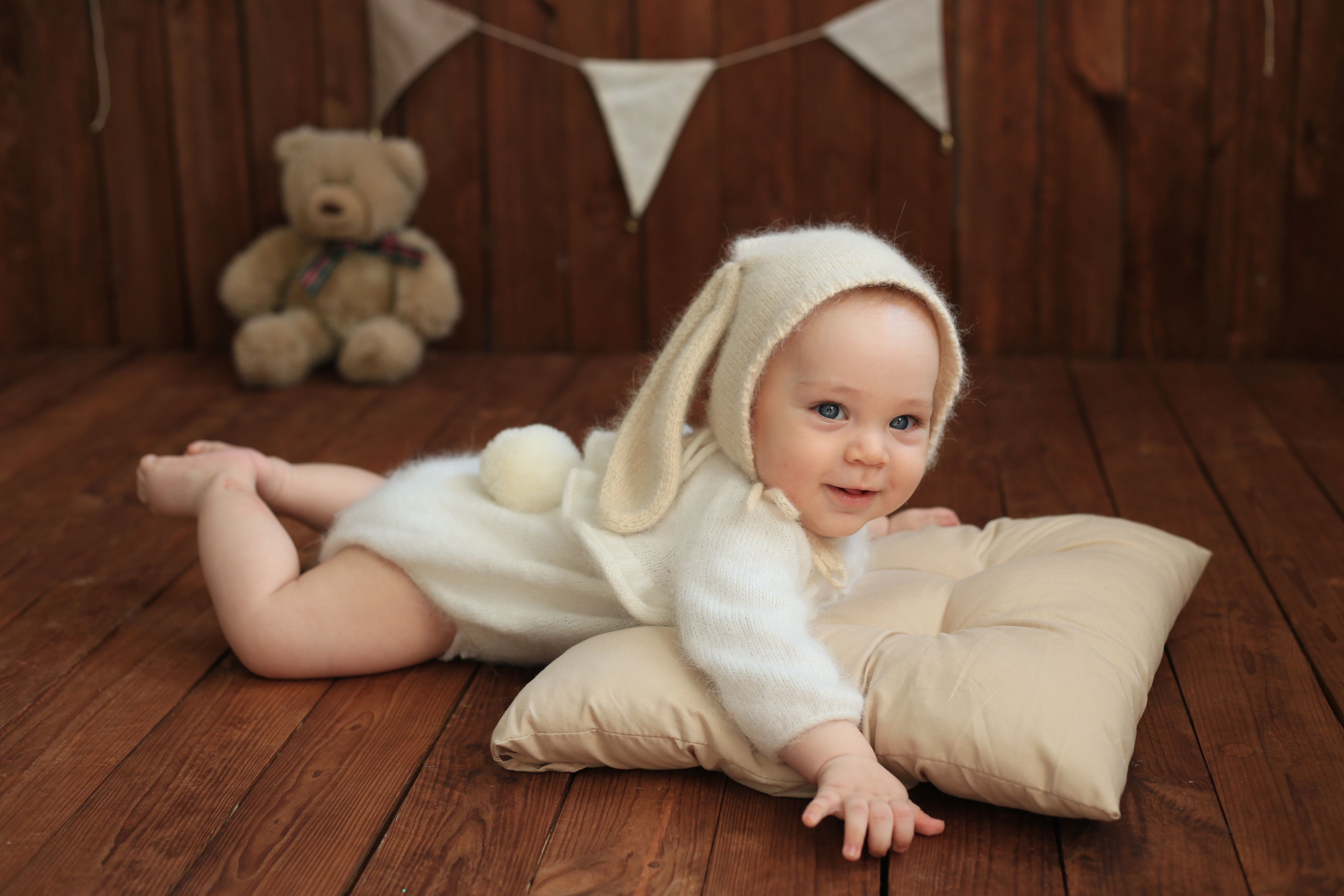 Cute baby dressed in a bunny suit relaxing on a pillow in a cozy wooden room.