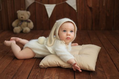 Free Cute baby in a bunny outfit lying on a soft pillow with a teddy bear in the background. Stock Photo