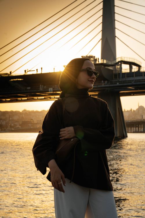 Free Stylish woman in sunglasses poses by a modern bridge at sunset in Istanbul, Turkey. Stock Photo