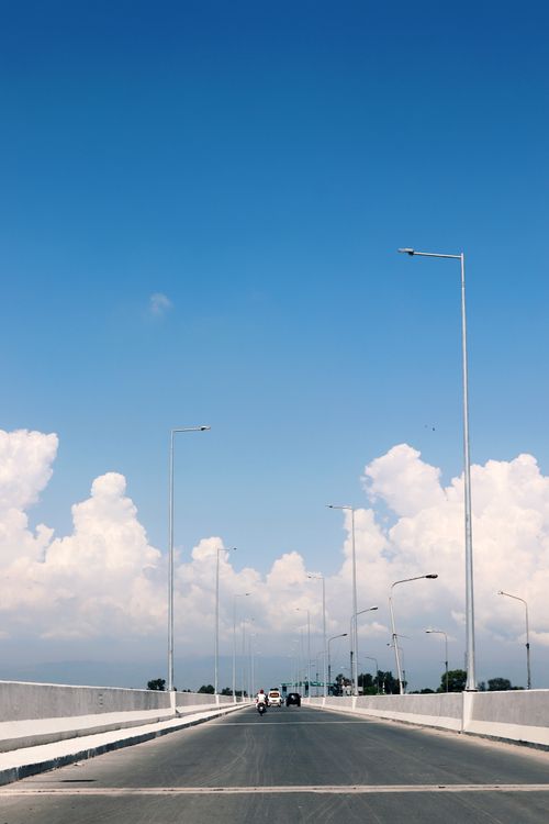 Free A serene open road in Sargodha, Pakistan, leading to the horizon under a clear blue sky with fluffy clouds. Stock Photo