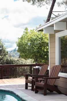 A serene backyard scene featuring wooden Adirondack chairs on a deck next to a swimming pool.