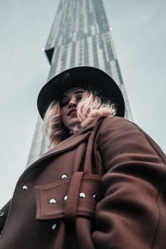 一位穿着棕色外套的时尚女性站在一栋高大的现代摩天大楼旁