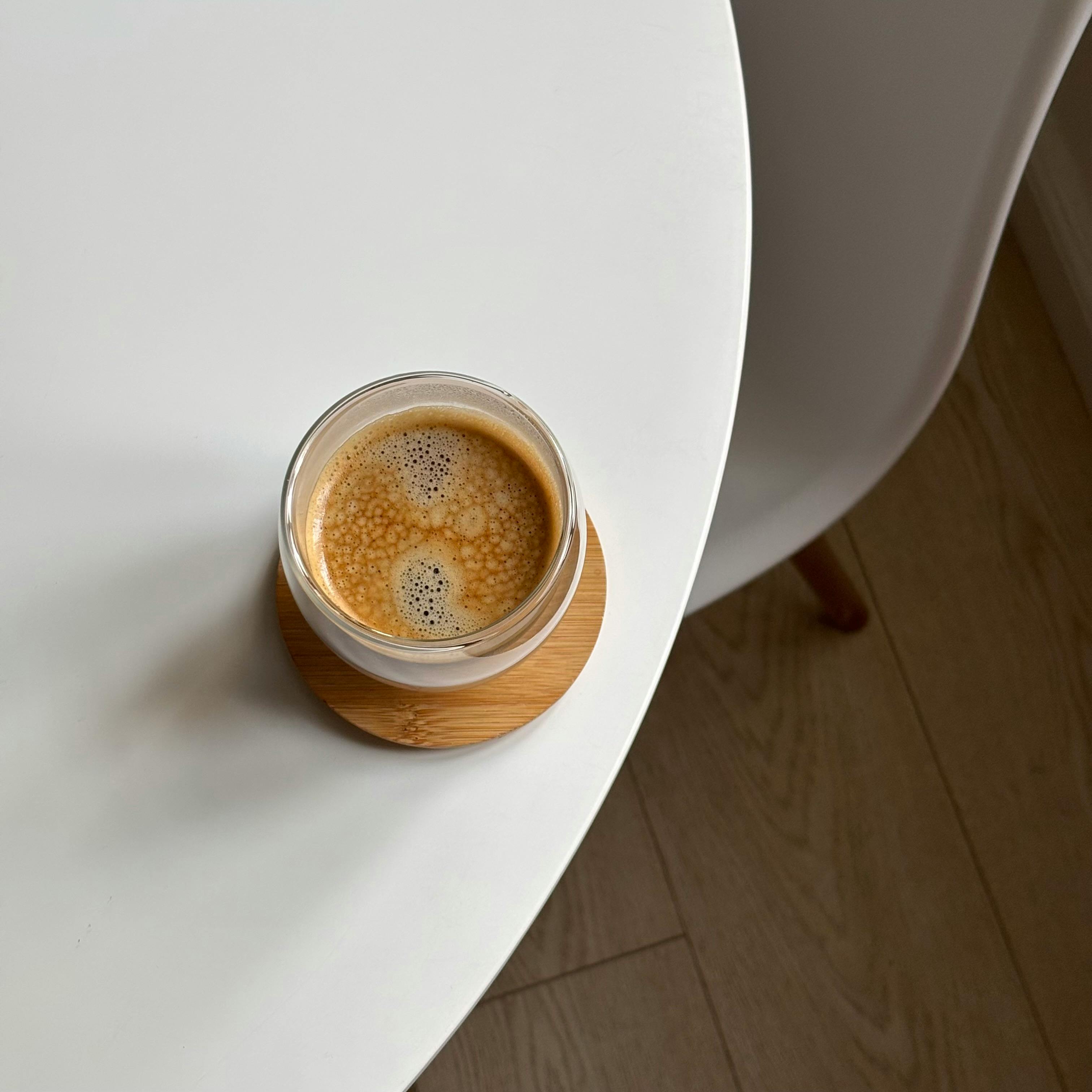 Top view of a coffee cup on a coaster, placed on a white table with a chair, showcasing minimalist design.