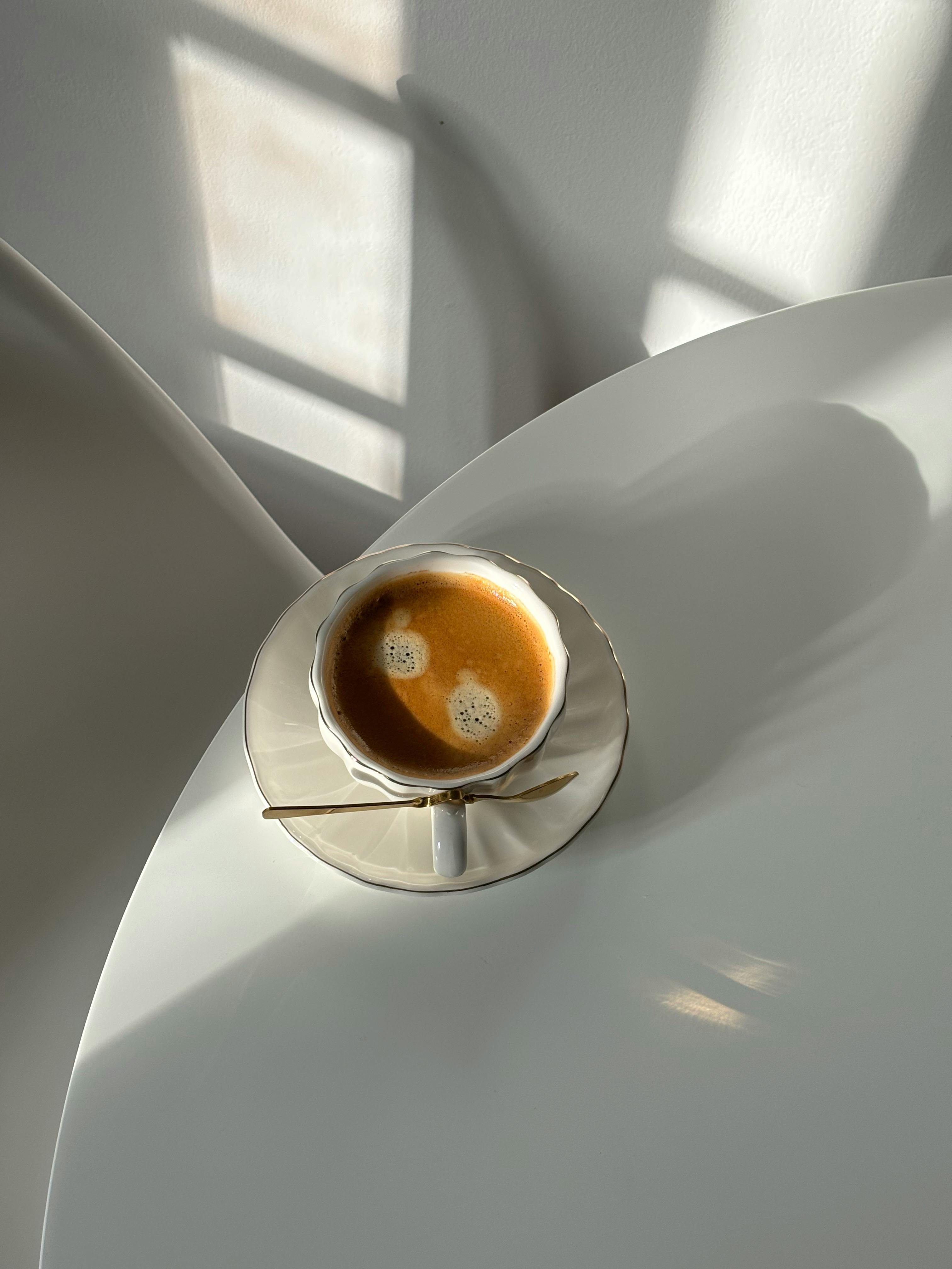 A minimalist shot of a coffee cup casting shadows on a sunlit white tabletop.
